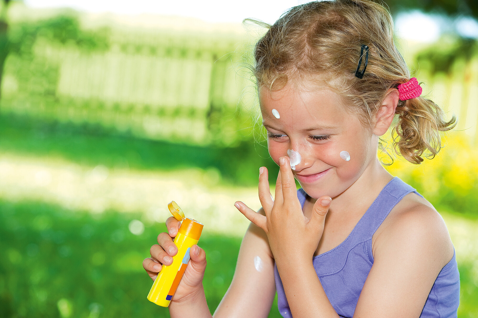 Mädchen reibt sich Sonnencreme ins Gesicht auf einer Wiese
