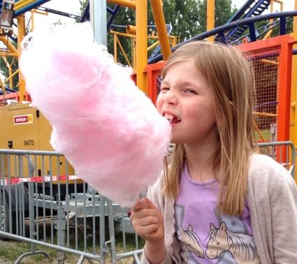 Süßes schmeckt! Mädchen isst Zuckerwatte vor einer Achterbahn